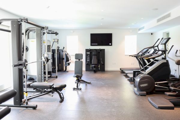 The image shows a modern gym with fitness equipment, including treadmills, weight machines, and benches, set in a well-lit room.