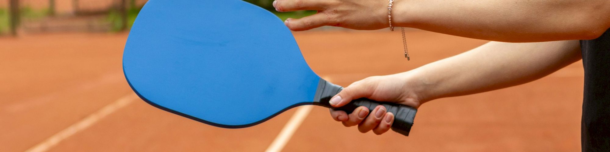 A person holding a blue pickleball paddle and a yellow pickleball, standing on a court near a net.