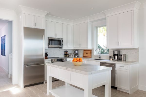 A modern kitchen with white cabinets, stainless steel appliances, and a central island with a bowl of oranges on top of it.