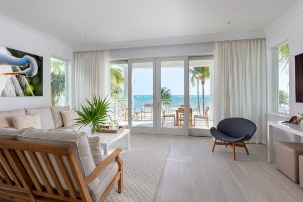 A bright and modern living room with wooden furniture, a TV, and a view of the ocean through large windows and sliding doors.