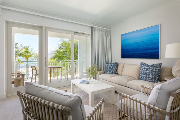 A bright, modern living room with a view of a balcony. Furnished with a beige sofa, decorative pillows, armchairs, a coffee table, and wall art.