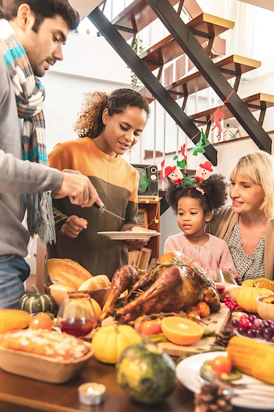 A group of people are gathered around a table enjoying a meal with a roasted turkey and various dishes, appearing to celebrate a festive occasion.