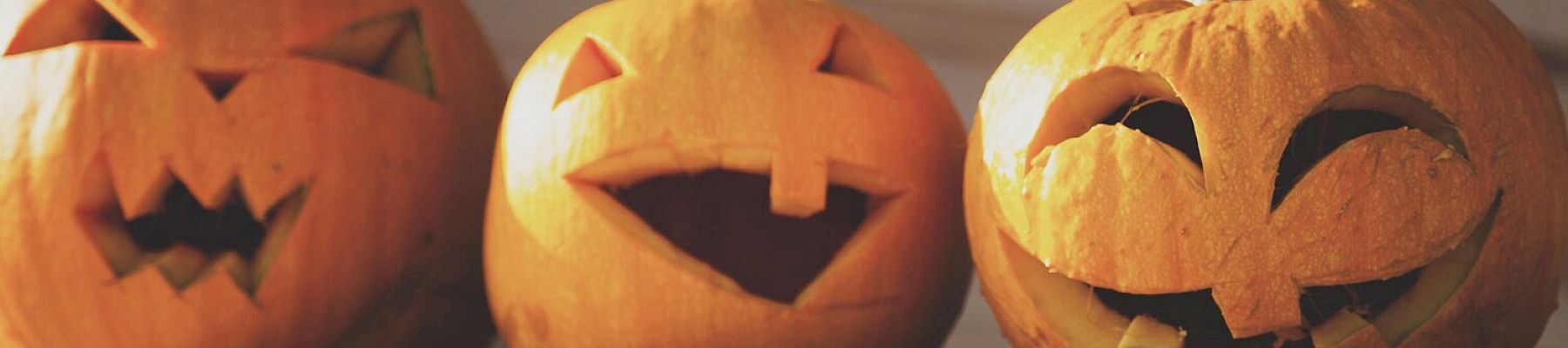 Three carved pumpkins with various facial expressions are placed side by side on a wooden surface, likely for Halloween.