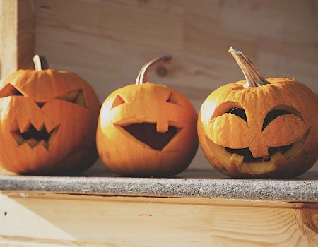 Three carved pumpkins with various facial expressions are placed side by side on a wooden surface, likely for Halloween.