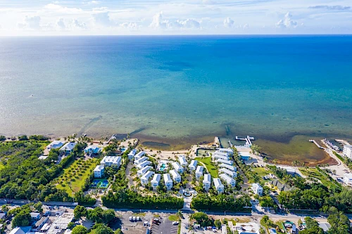 An aerial view of a coastal resort with white buildings, green landscapes, and a deep blue ocean horizon in the background.