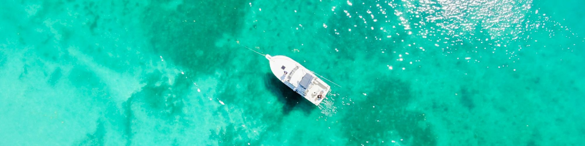 Aerial view of a boat floating on clear turquoise water, with sunlight creating a bright reflection on the surface.