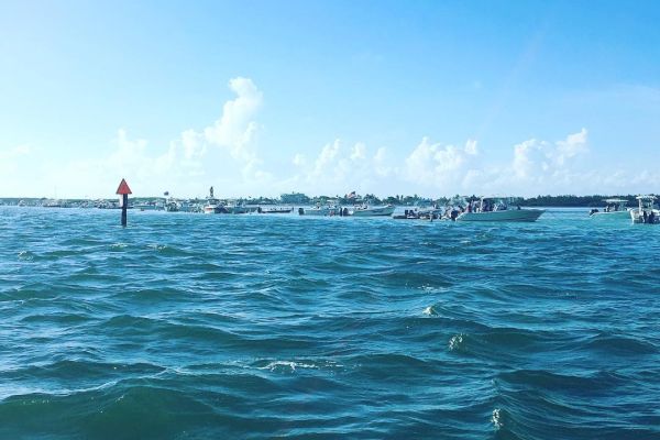 The image shows a vast expanse of water under a clear blue sky, with distant boats and a navigation marker visible in the background.