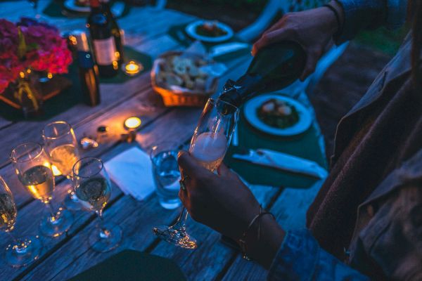 A person is pouring champagne into a glass at a candlelit table arranged with glasses, plates, and a basket of bread, creating an elegant setting.