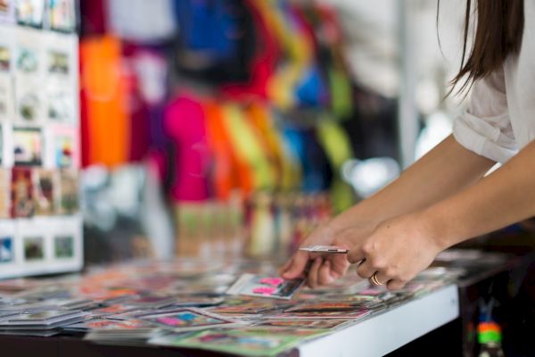 A person is browsing through a collection of colorful photographs or postcards on a table, with vibrant clothing in the background.