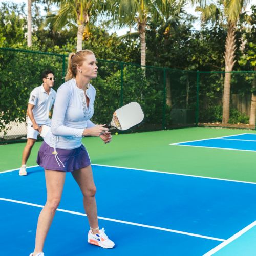 Two people are playing pickleball on an outdoor court, with one person preparing to hit the ball and the other standing behind them.