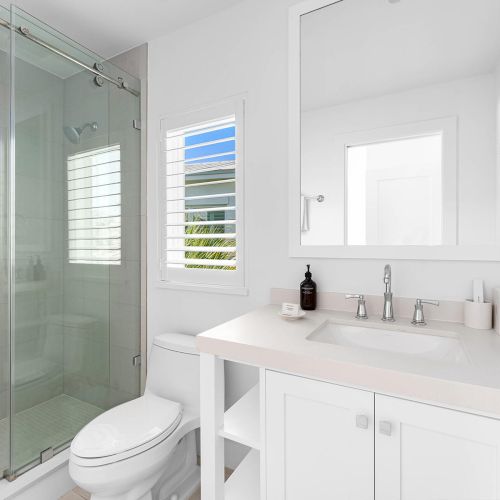 A modern bathroom with a glass shower, toilet, and sink set in a white vanity. A mirror and toiletries are placed on the countertop.