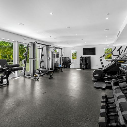 The image shows a gym with various fitness equipment, including treadmills, weights, and resistance machines, in a well-lit room.