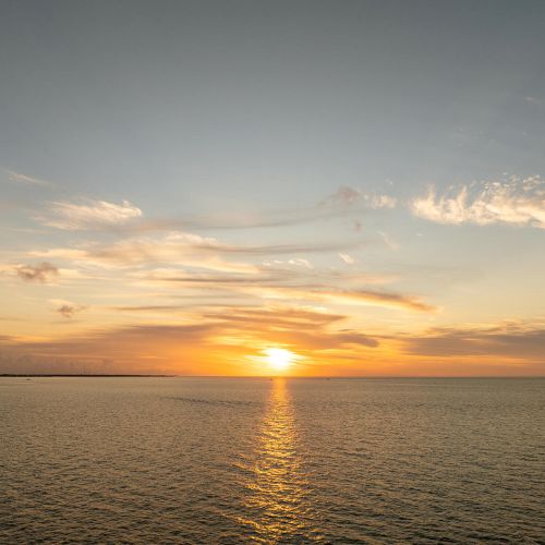 A serene sunset over calm ocean waters, with scattered clouds and a horizon line in the distance enhancing the tranquil scene.