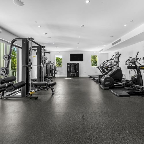 A modern gym with various exercise machines, including treadmills, ellipticals, and weight equipment, in a bright, spacious room.