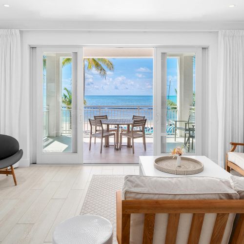 A bright living room with a beach view through sliding glass doors, featuring modern furniture and a small outdoor patio setup.