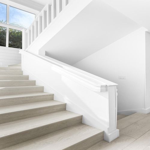 The image shows a modern, white staircase with wooden steps, large window, and minimalist decor.