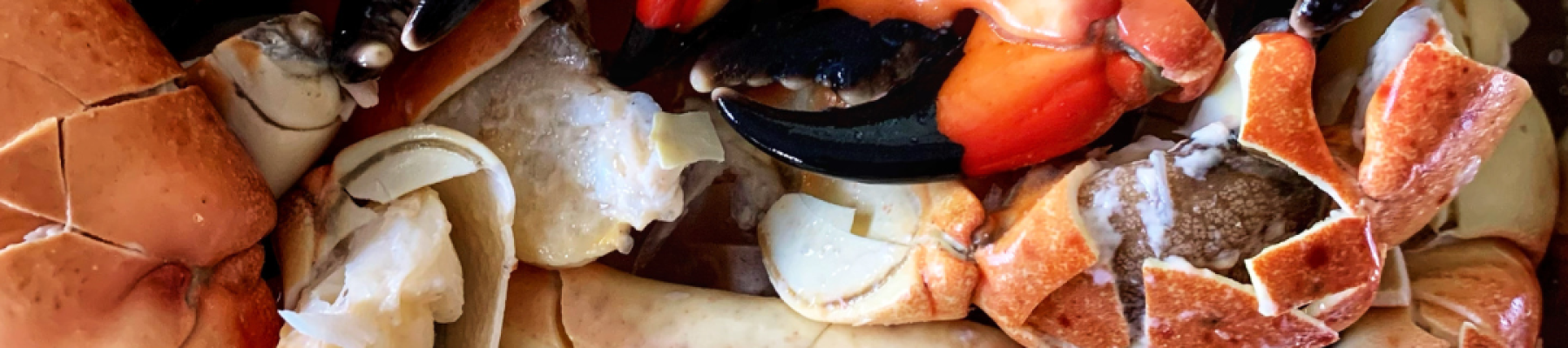 A pile of stone crab claws in various shades of orange and black, arranged closely together, ready for a seafood feast.