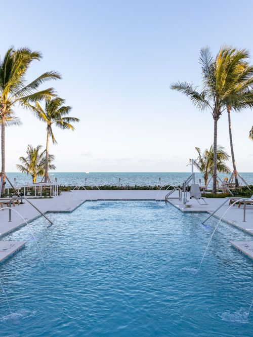 A serene poolside view with lounge chairs, palm trees, and ocean in the background, creating a tropical and relaxing atmosphere.